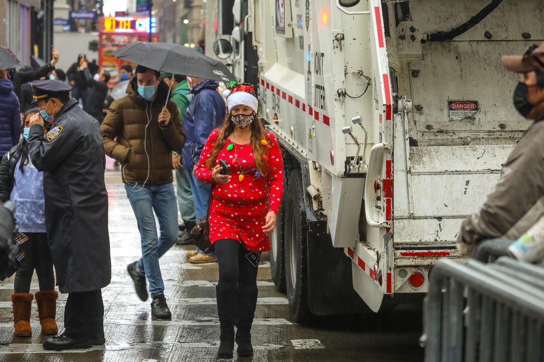 A woman dressed in a Santa-style dress walks by a sanitation truck